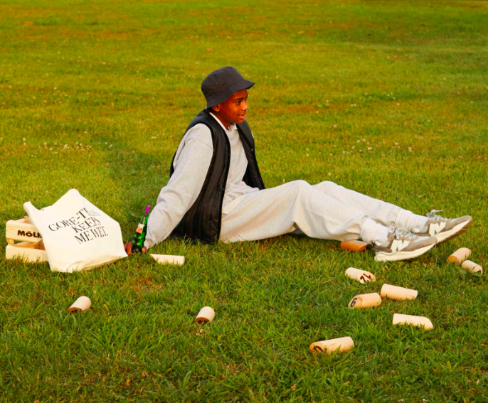 a boy sitting on the grass newx to a molkky game