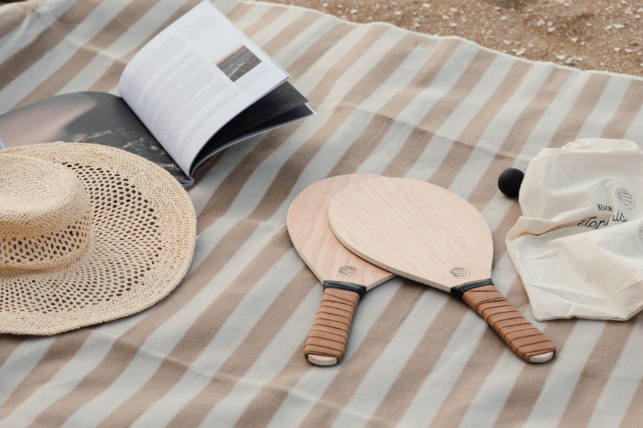 two beach rackets, a book and a hat on a beach towel